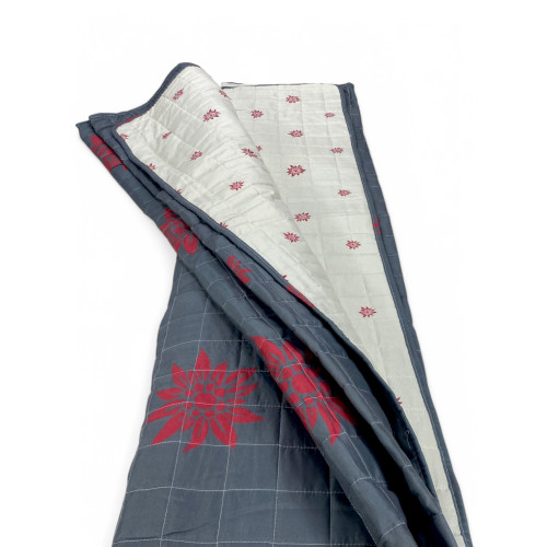 Colcha Edelweiss plegada con interior claro y diseños rojos